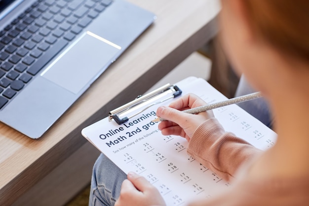 High angle close up of unrecognizable kid doing math test for online school while studying at home, copy space