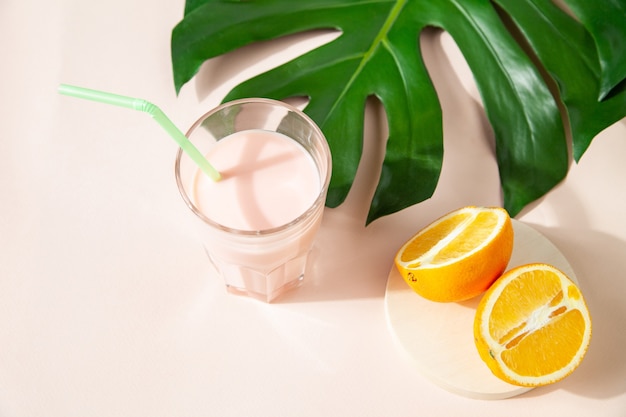 High angle of fresh sweet smoothie in glass placed on table with halves of orange and monstera leaf in studio on green background