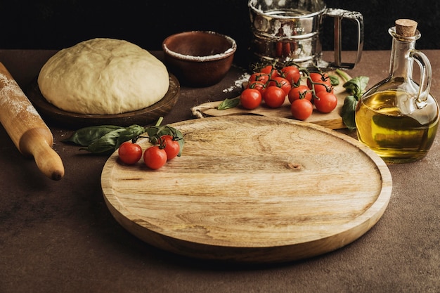 High angle of pizza dough with wooden board and tomatoes