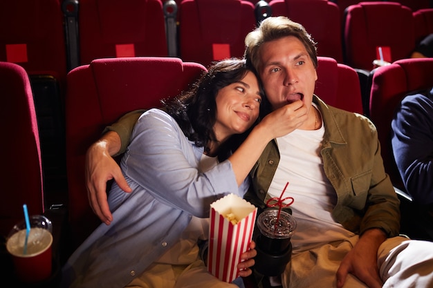 High angle portrait of carefree young couple watching movie in cinema theater and eating popcorn, copy space