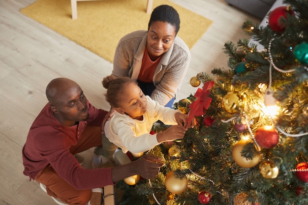 High angle portrait of cute African-American girl decorating Christmas tree with loving family while enjoying holiday season at home