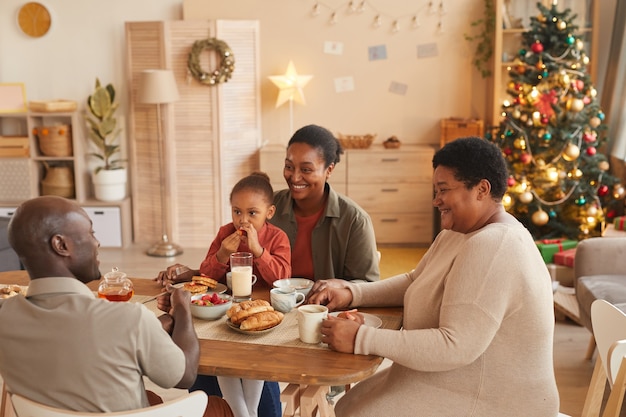 High angle portrait of happy African-American family enjoying tea and snacks while celebrating Christmas at home