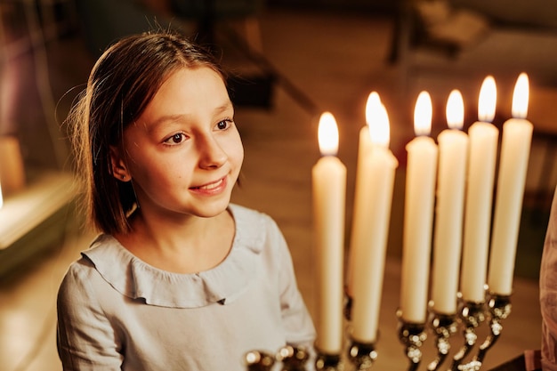 High angle portrait of smiling jewish girl looking at menorah candle during hanukkah celebration