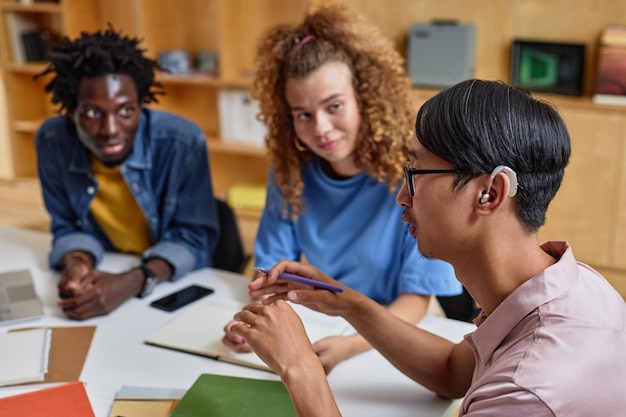 High angle portrait of young asian man speaking to group of students in library copy space