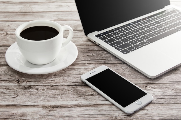 High angle shot of a cup of coffee, laptop, and a smartphone on a wooden surface