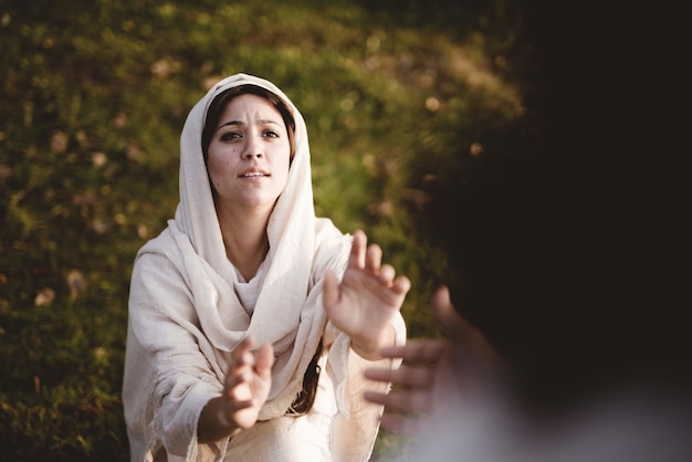 High angle shot of a Female wearing a biblical robe and reaching for help from Jesus Christ