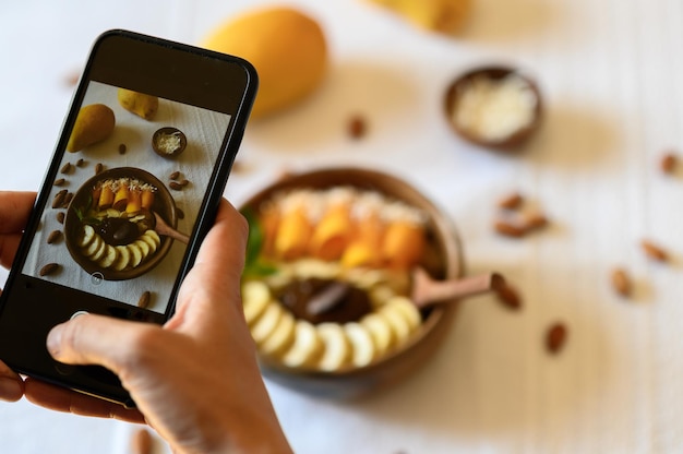 Photo high angle soft focus of crop anonymous blogger taking photo on smartphone of delicious bowl with sweet fruits for social media