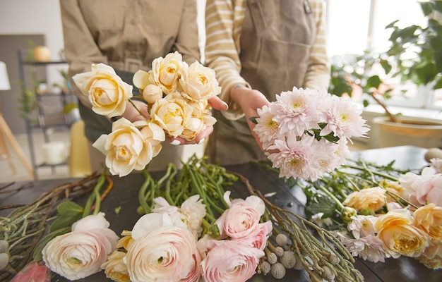 High angle view at beautiful flowers on table in flower shop with two unrecognizable florists arranging bouquets, copy space