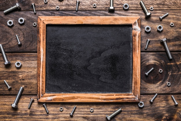 High angle view of blank slate surrounded by bolts and nuts