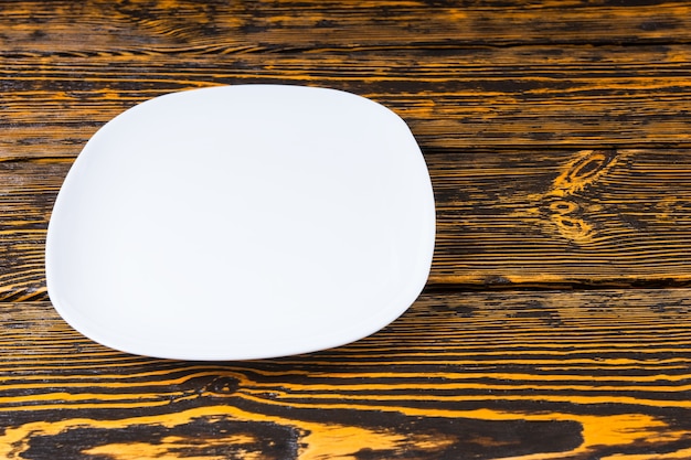 High angle view of an empty plain white ceramic plate on a textured wood background with copyspace for placement of your food or product