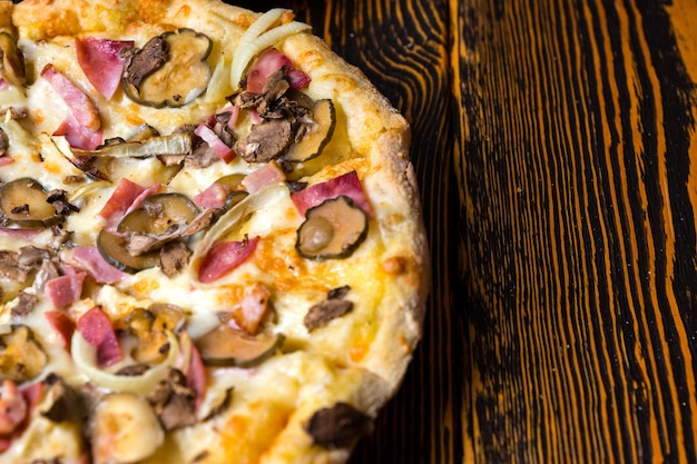 High angle view of half of tasty pizza with ham, mushrooms, onion and pickles on wooden table