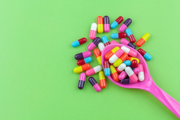 High angle view of multi colored pills in spoon over green background