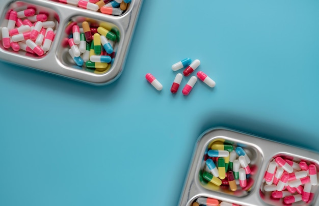 High angle view of multicolored antibiotic capsule pills on stainless steel tray and blue background