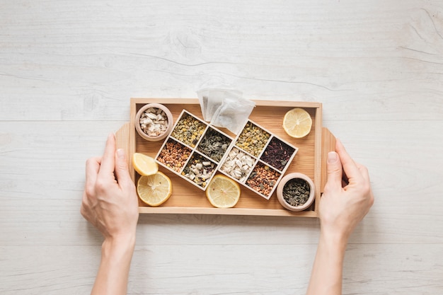 High angle view of a person's hand holding wooden tray with herbs and dry tea leaves