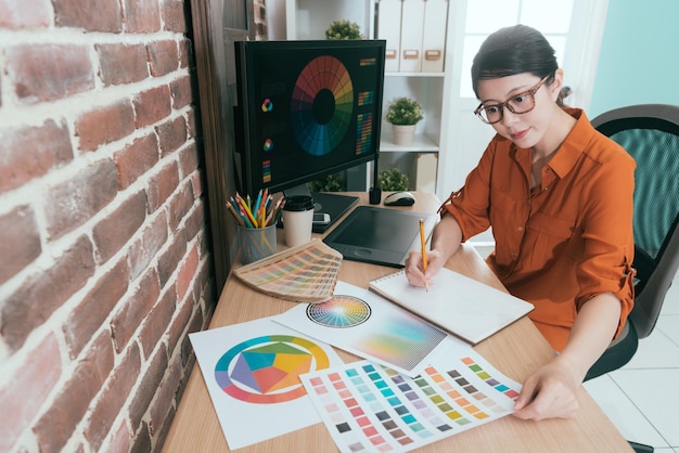 high angle view photo of attractive smiling designer looking at colorful paper choosing right color in order to sketching craft.