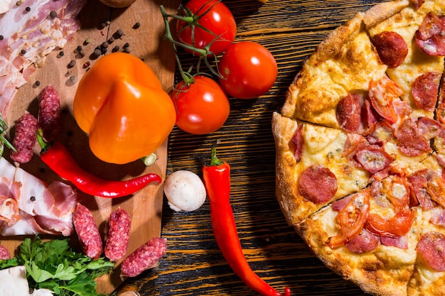 High angle view of pizza on wooden table, near lie vegetables, mushrooms and cutting board with meat