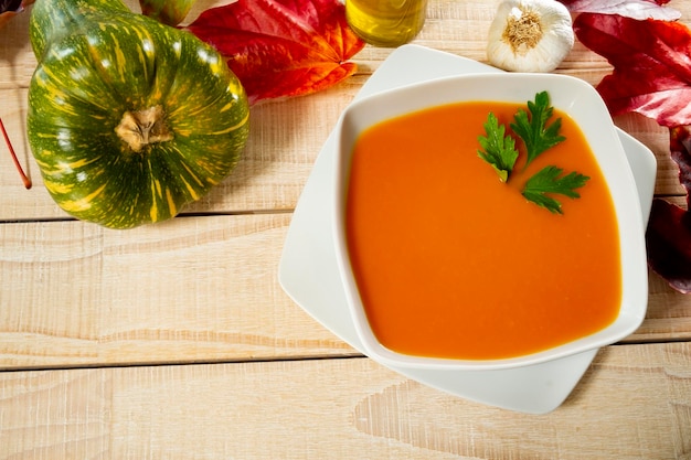 High angle view of pumpkin soup served in bowl with autumn leaves on table.