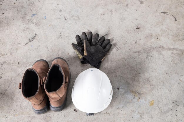 Photo high angle view of safety shoes glove and white hardhat on cement floor