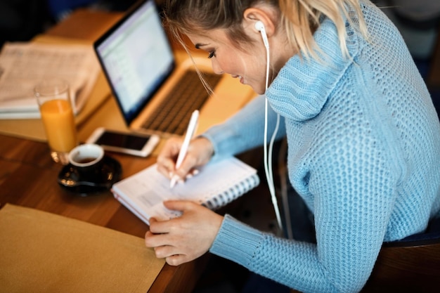 High angle view of smiling freelancer writing to do list in her weekly planner while working in cafeteria