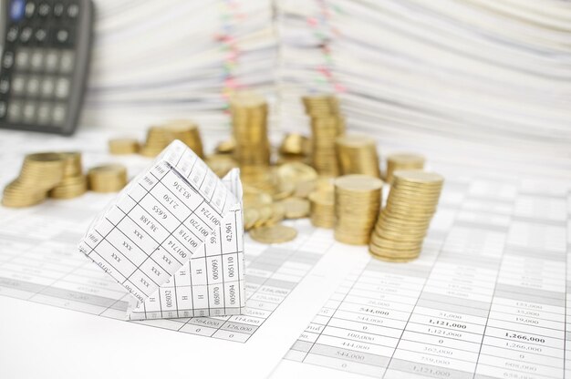 High angle view of stacked coins with fallen model house and calculator on financial documents