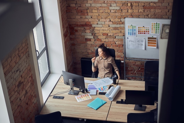 Photo high angle view of thoughtful interior designer woman looking at the window holding glasses