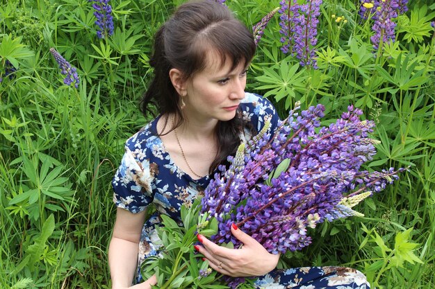 Photo high angle view of woman with lavenders looking away while sitting on grassy field