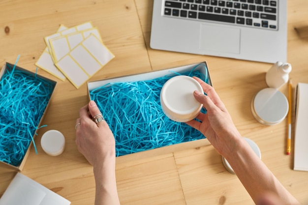 High angle view of woman working with online orders she putting cream in cardboard box