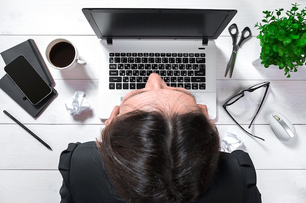 High angle view of an young brunette working at her office desk with documents and laptop. Businesswoman working on paperwork.