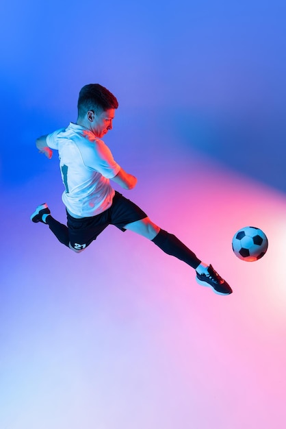 High angle view of young man male soccer football player training isolated on gradient blue pink background in neon light