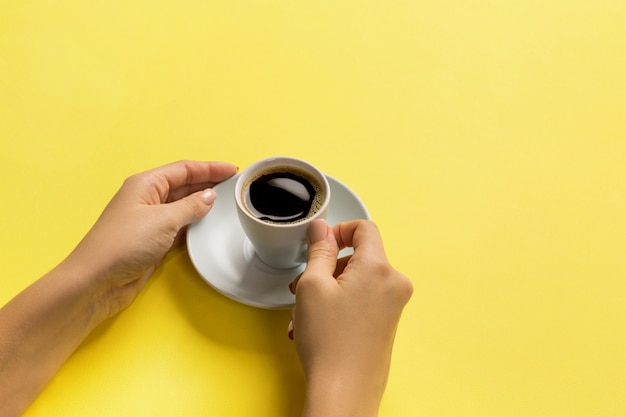 High angle of woman hands holding coffee cup on yellow surface 