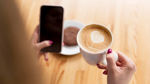 High angle of woman having coffee while holding smartphone