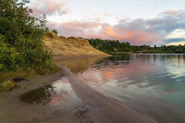 A high cliff on the shore of a lake with colorful clouds in the sky at sunset