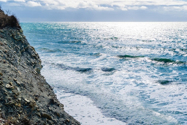 High cliffs and a pebbly beach below Beautiful storm waves in foam hit the beach