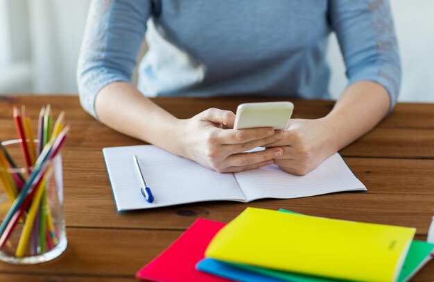 high school, education, people and learning concept - close up of young student or woman with smartphone and book writing to notebook at home