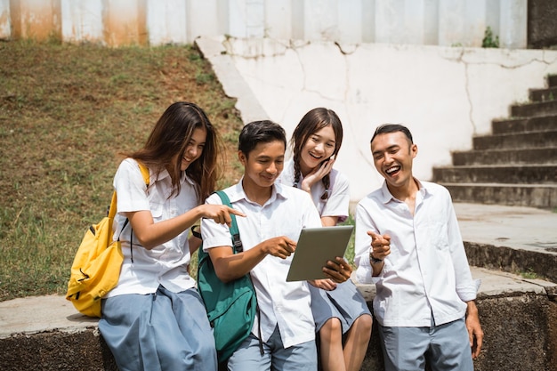 High school student laughs at the sight and points at the tablet screen while hanging out with his f