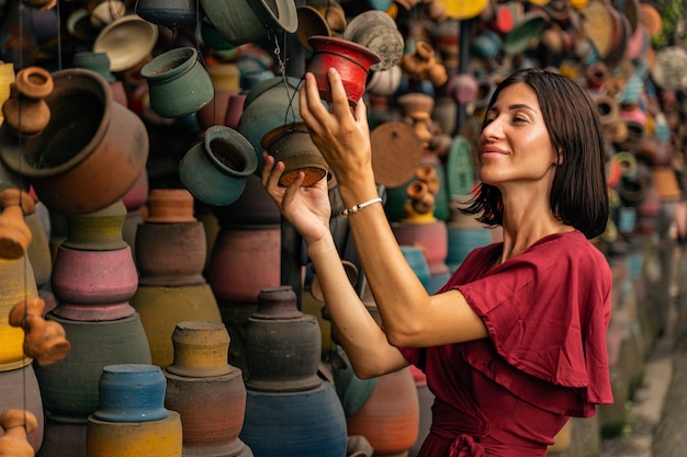 High spirits. Pleased young female person standing in semi position and looking at colorful pottery