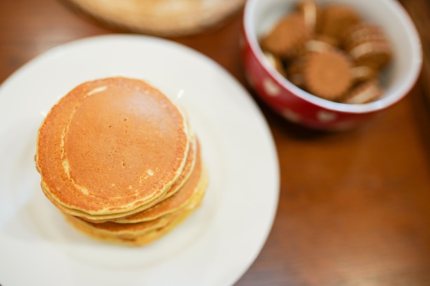 High stack of pancakes on white plate on wooden table in the kitchen 