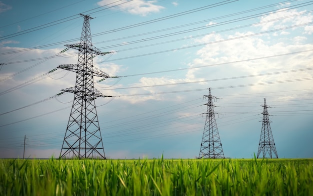 High voltage lines and power pylons in a flat and green agricultural landscape on a sunny day with clouds in the blue sky. Cloudy and rainy. Wheat is growing