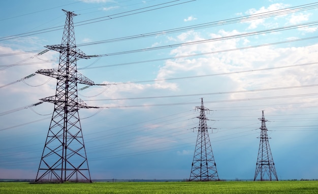 High voltage lines and power pylons in a flat and green agricultural landscape on a sunny day with clouds in the blue sky. Cloudy and rainy. Wheat is growing