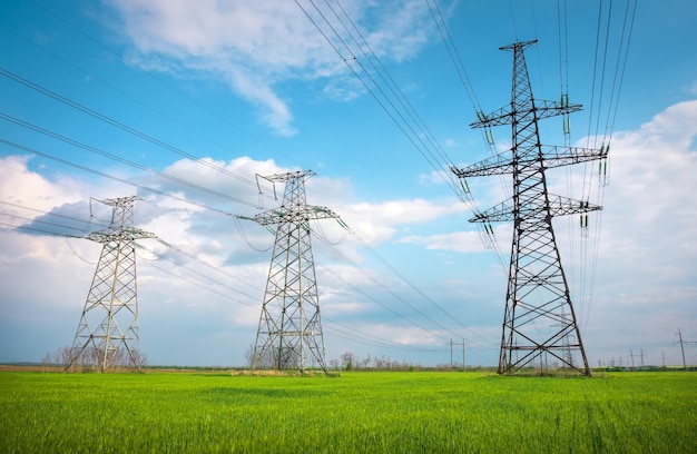 High voltage lines and power pylons in a flat and green agricultural landscape on a sunny day with clouds in the blue sky Cloudy and rainy Wheat is growing