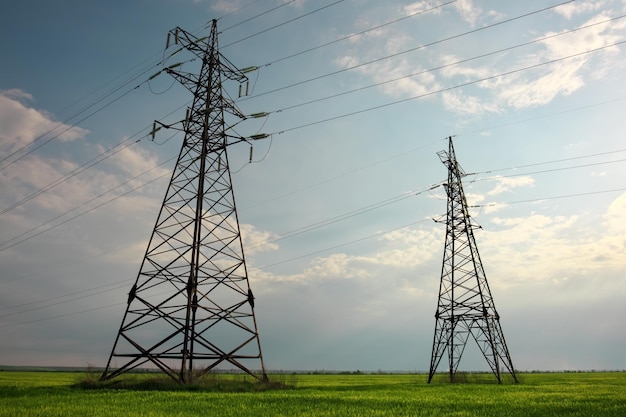 High voltage lines and power pylons in a flat and green agricultural landscape on a sunny day with clouds in the blue sky Cloudy and rainy Wheat is growing