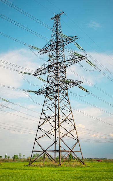 High voltage lines and power pylons in a flat and green agricultural landscape on a sunny day with clouds in the blue sky Cloudy and rainy Wheat is growing