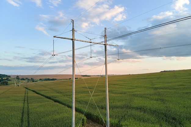 High voltage tower with electric power lines between green agricultural fields Transfer of electricity concept