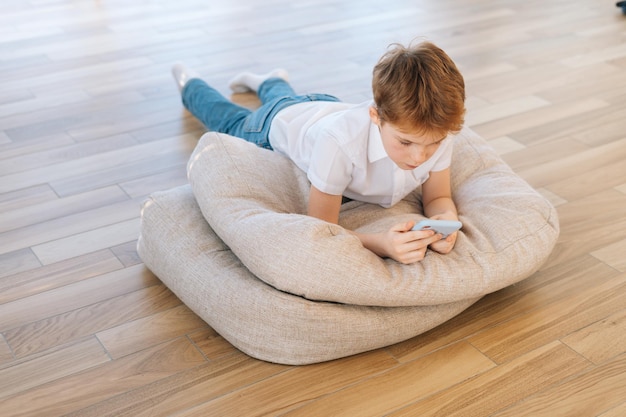 Highangle view of cute little child boy relaxing lying on pillow enjoying leisure time with mobile phone chatting on social media