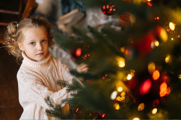 Highangle view of pretty little blonde curly child girl decorating christmas tree with festive balls