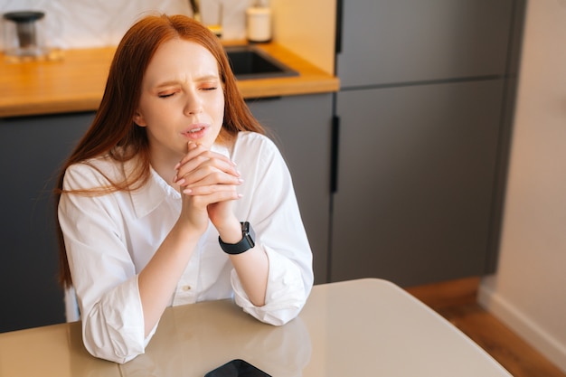 Highangle view of sad young woman praying with eyes closed holding folded hands in front of face at