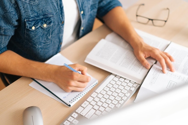 Highangle view of unrecognizable male student studying online from home using computer writing notes watching video class lesson