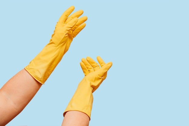 Highlight women's hands in yellow rubber gloves on a blue background of copyspace House cleaning