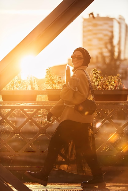 A hijab woman in stylish sunglasses and an elegant french outfit walking through the city at sunset