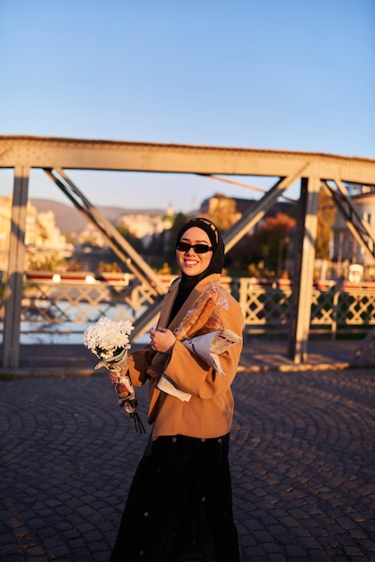 A hijab woman in stylish sunglasses and an elegant french outfit walking through the city at sunset